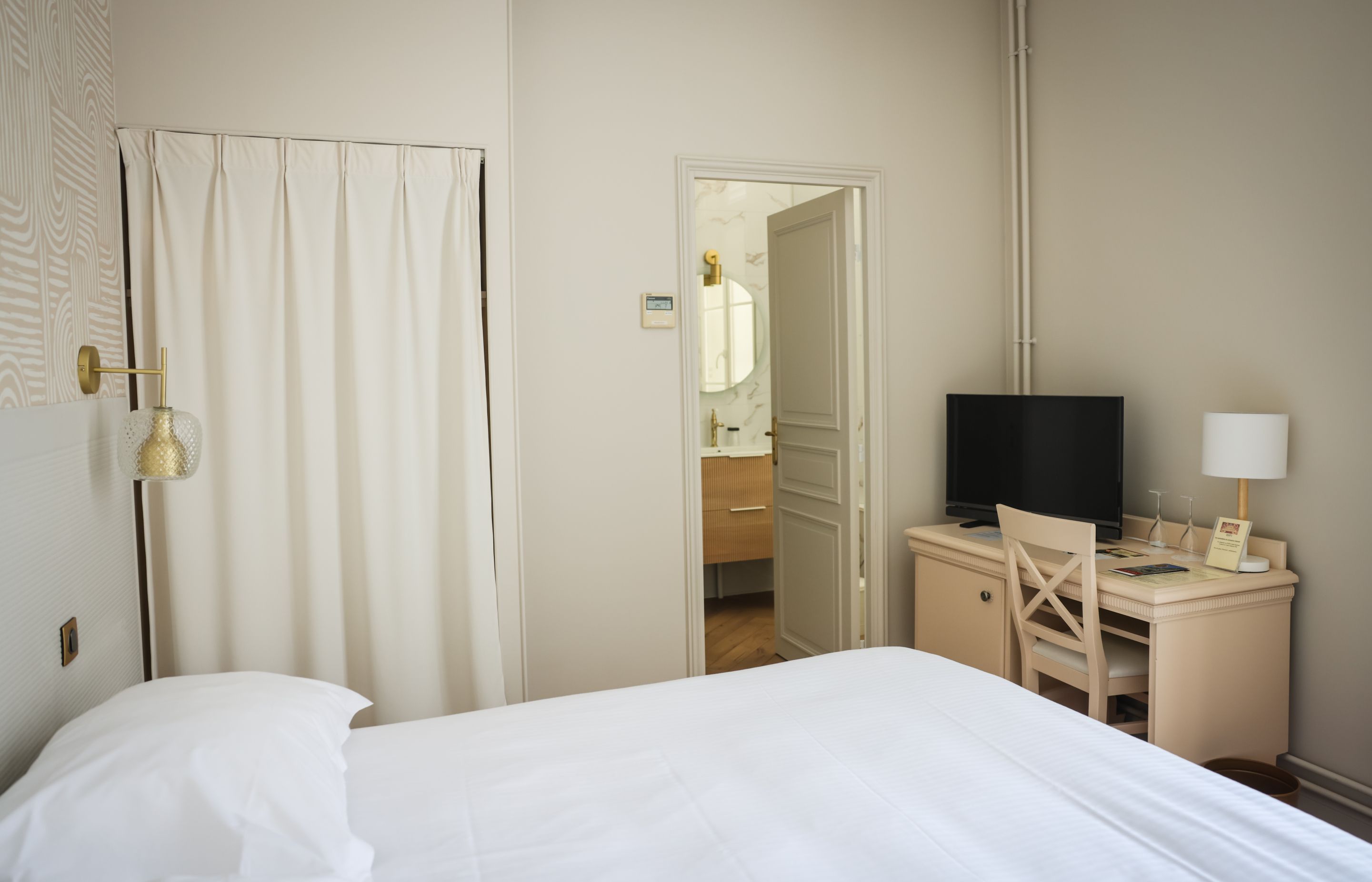 A hotel room with a bed, a desk with a television, and a bathroom visible through an open door.
