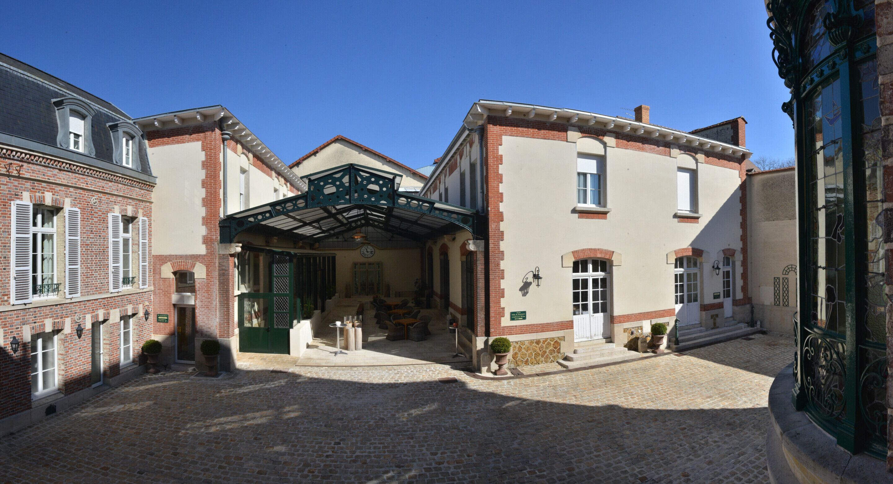 A courtyard with a covered seating area, a brick building, and a green metal bridge.