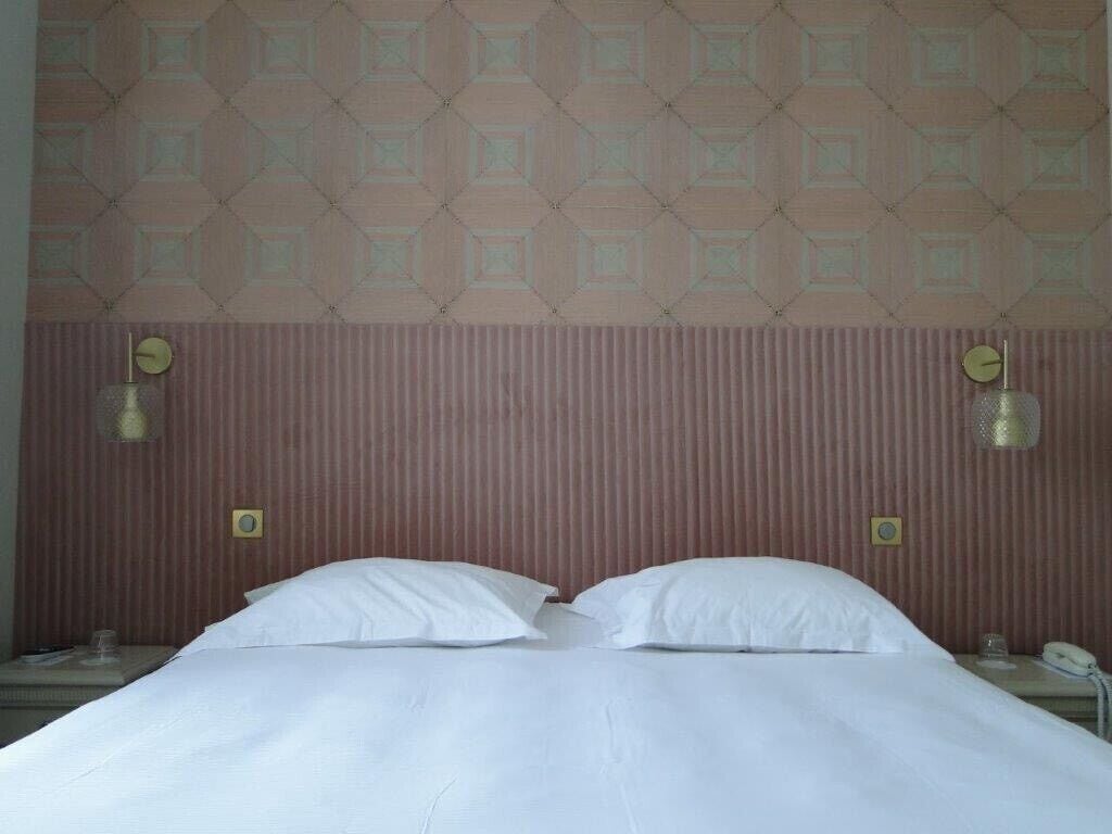 A hotel room with a bed, two bedside lamps, a telephone, and a wall with a geometric pattern.