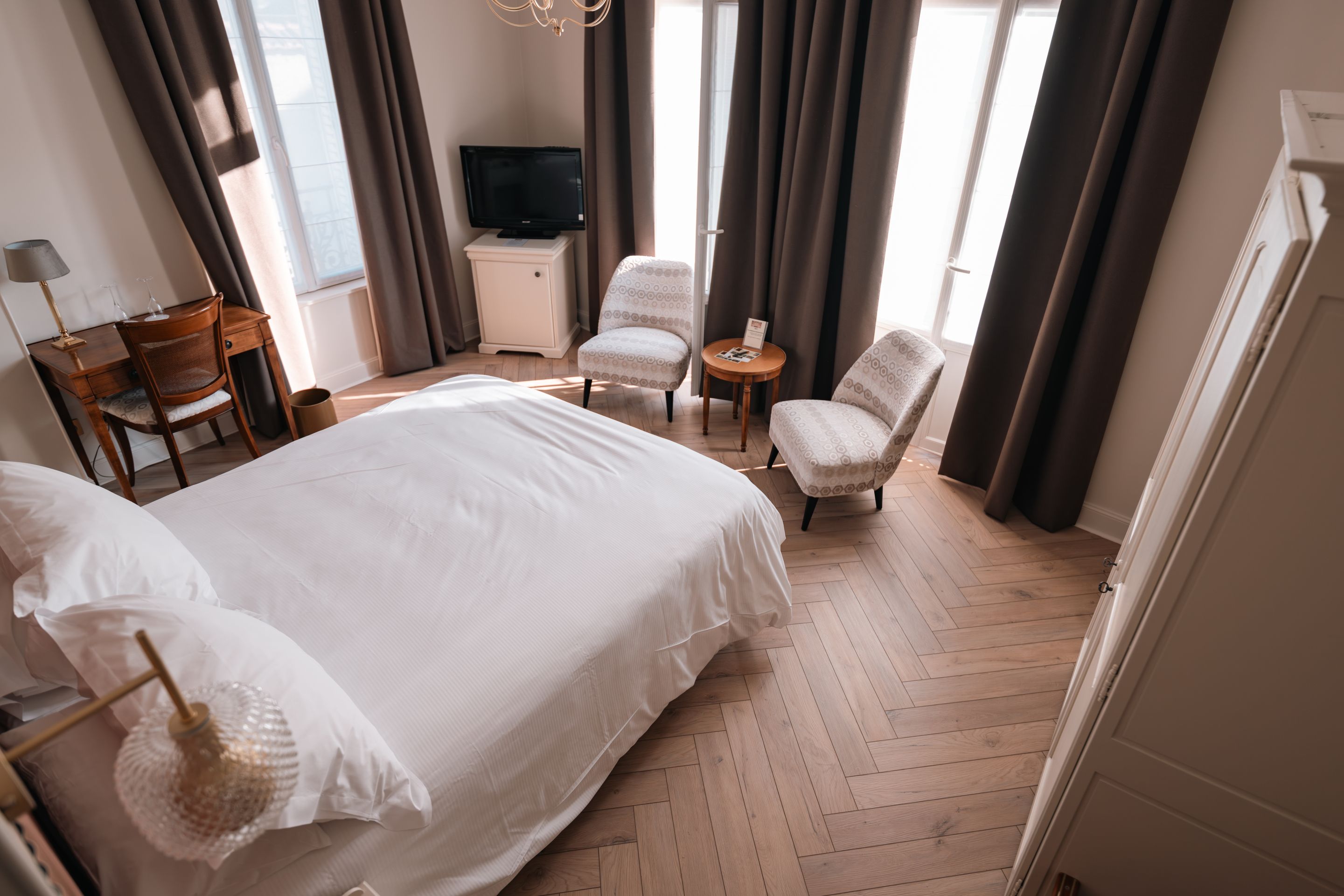 A hotel room with a large bed, a desk, a chair, a television, and a small table.