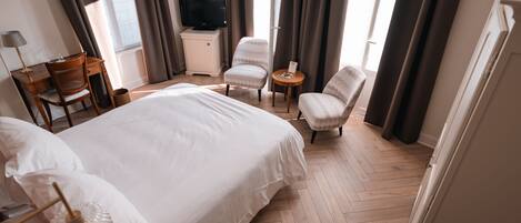 Habitación de hotel con una cama grande, un escritorio, una silla, un televisor y una mesita.