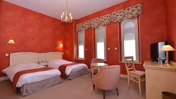 A hotel room with two beds, a desk, a chair, a television, and a chandelier.