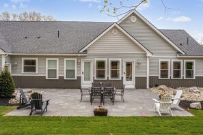 Ein zweistöckiges Haus mit überdachter Terrasse, Sitzgelegenheit im Freien und einem kleinen Garten.