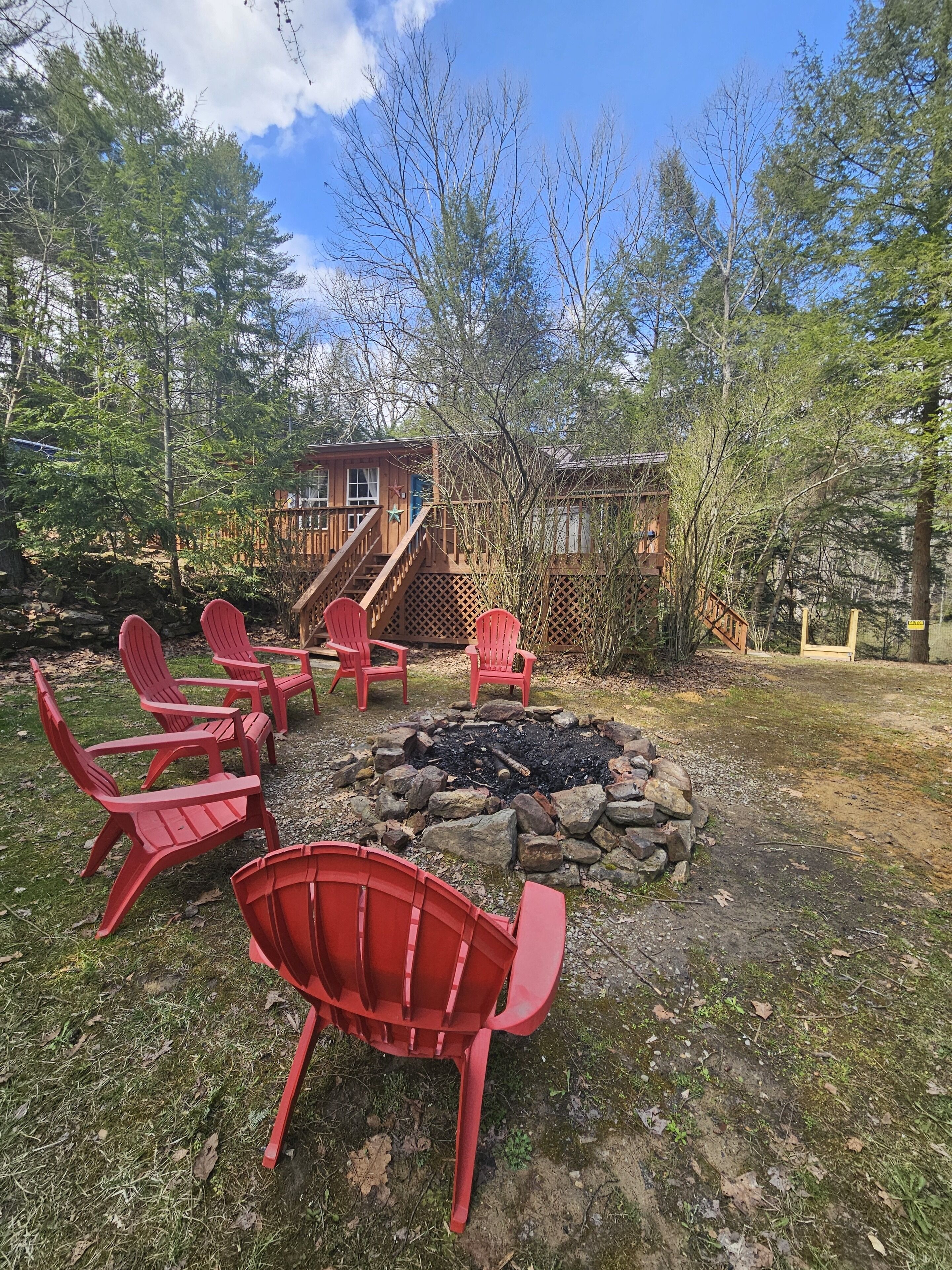 Una cabaña de madera con un brasero y sillas Adirondack rojas en un área boscosa.