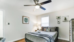Ein Schlafzimmer mit Bett, Deckenventilator, Fenster und Nachttisch mit Lampe.