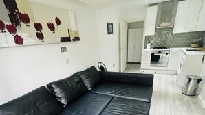 Un espace de vie moderne avec un canapé en cuir noir, une table à manger et une cuisine en arrière-plan.