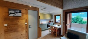 Una habitación acogedora con una puerta de madera, una zona de comedor con mesa y sillas, y vistas a una cocina y un balcón.