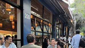 An outdoor dining area with tables and chairs, a number '200' on a pillar, and people dining.