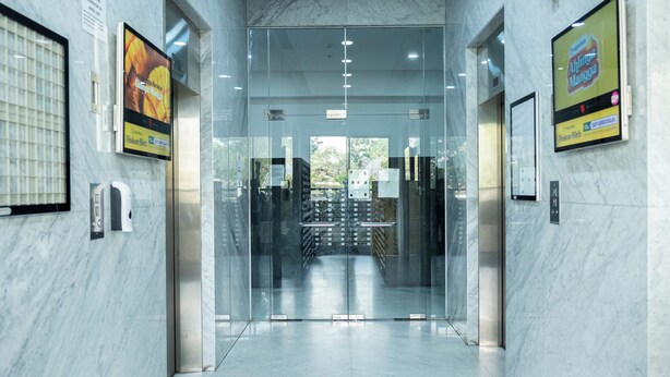 A modern elevator with glass doors, marble walls, and digital signage advertising a local restaurant. - Nusantara Rooms By Reccoma (Bekasi)