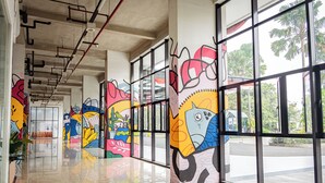 A corridor with colorful murals on the walls, large windows, and a tiled floor. - Nusantara Rooms By Reccoma (Bekasi)