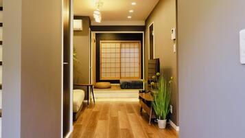 A hallway with wooden flooring, recessed lighting, a sliding door with a grid pattern, a bench, and a potted plant.