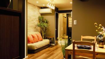A modern living room with a sofa, a dining table with chairs, a clock on the wall, and a plant.