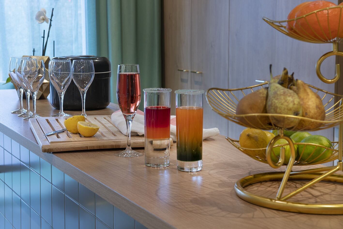 A bar area with multiple glasses of beverages, a fruit basket, and a cutting board with lemons.