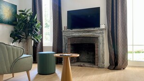 A modern living room with a fireplace, a flat-screen TV, a green armchair, and a round wooden coffee table. - Résidence DOMITYS - Les Séquanes (Chalon-sur-Saone)