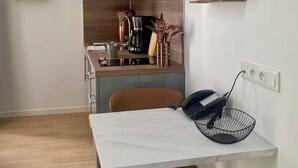 A modern kitchen with a dining area, featuring a marble table, a brown chair, and a black telephone. - Résidence DOMITYS - Les Séquanes (Chalon-sur-Saone)