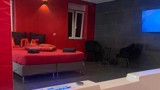 A modern room with a red accent wall, a bed with red pillows, a small table with a remote control, and a bathtub with water. - Loft 55 m2 Jacuzzi Billard Terrasse 15 min Hyper Centre Strasbourg (Hœnheim)