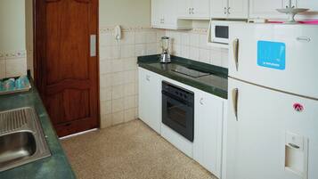Una cocina con gabinetes blancos, microondas, licuadora y refrigerador.