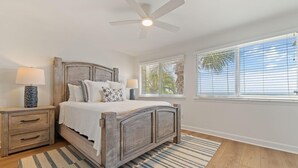 A bedroom with a wooden bed, two bedside tables with lamps, a ceiling fan, and a large window with blinds. - Needle Rush Point D11 (Pensacola)
