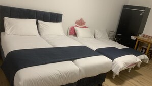 Een tweepersoonsbed met witte en marineblauwe beddengoed, een donker hoofdbord en een klein nachtkastje met een lamp.