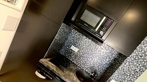 A modern kitchen with a black microwave, stainless steel appliances, and a tiled backsplash.