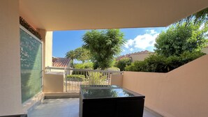 A balcony with a glass-top table, a white railing, and a view of trees and buildings.