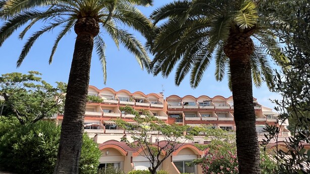 A multi-story hotel with balconies, surrounded by palm trees and greenery.