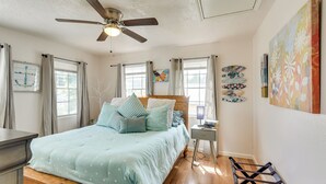 A bedroom with a bed, a nightstand, a desk, a chair, a ceiling fan, and artwork on the walls. - 3 Mi to Boardwalk: Bacliff Apartment w/ Hot Tub (Bacliff)