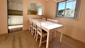 A dining area with a white table and chairs, a window with a view, and a kitchen visible through an archway. - Antibes - 4 people - Parking (Antibes)