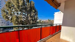 A balcony with a red safety fence, a tiled floor, and a view of a tree and buildings in the background. - Antibes - 4 people - Parking (Antibes)