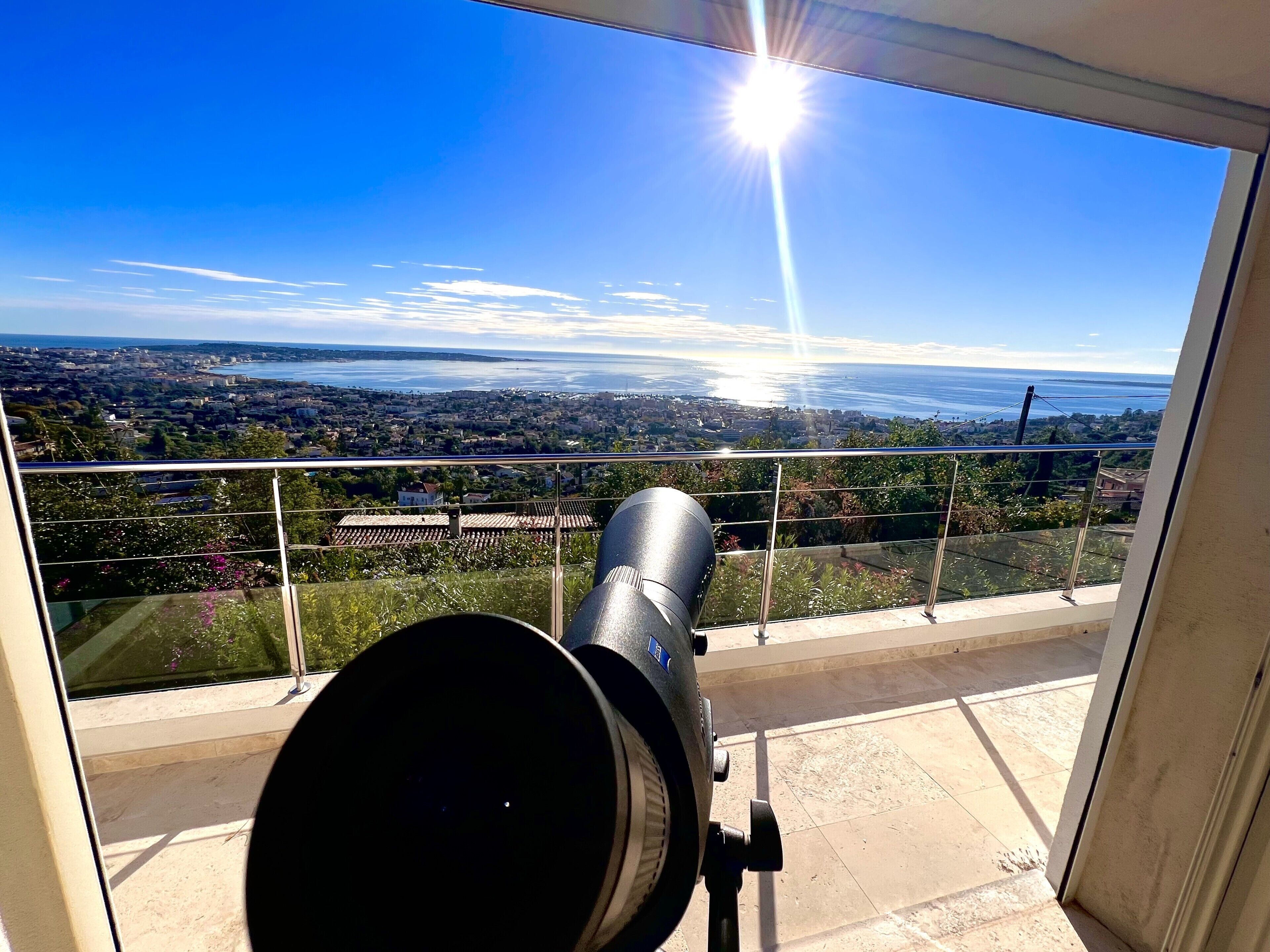 A telescope on a balcony overlooking a cityscape with a clear sky.