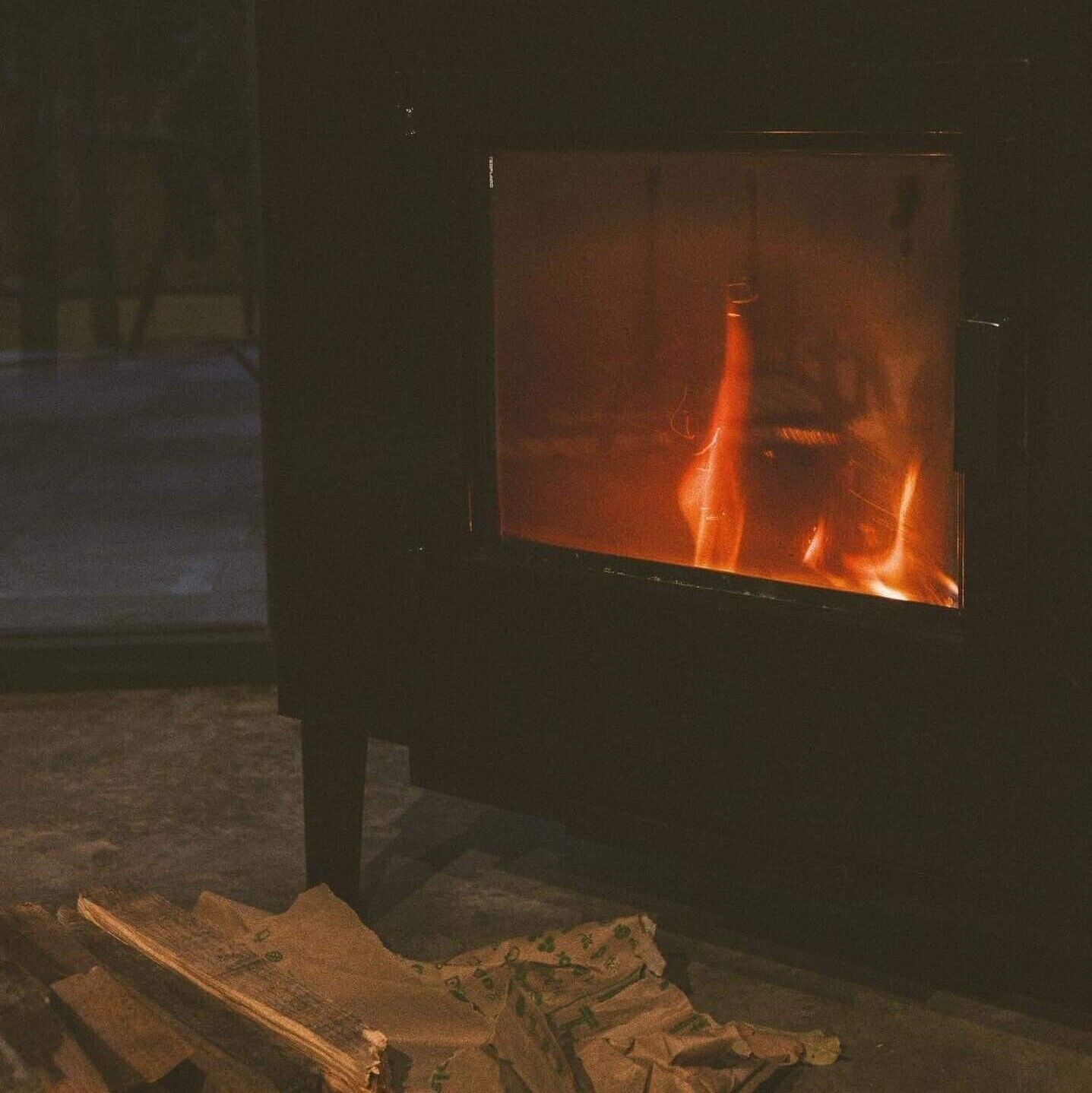 Una habitación con chimenea de leña, ventana y suelo de madera.