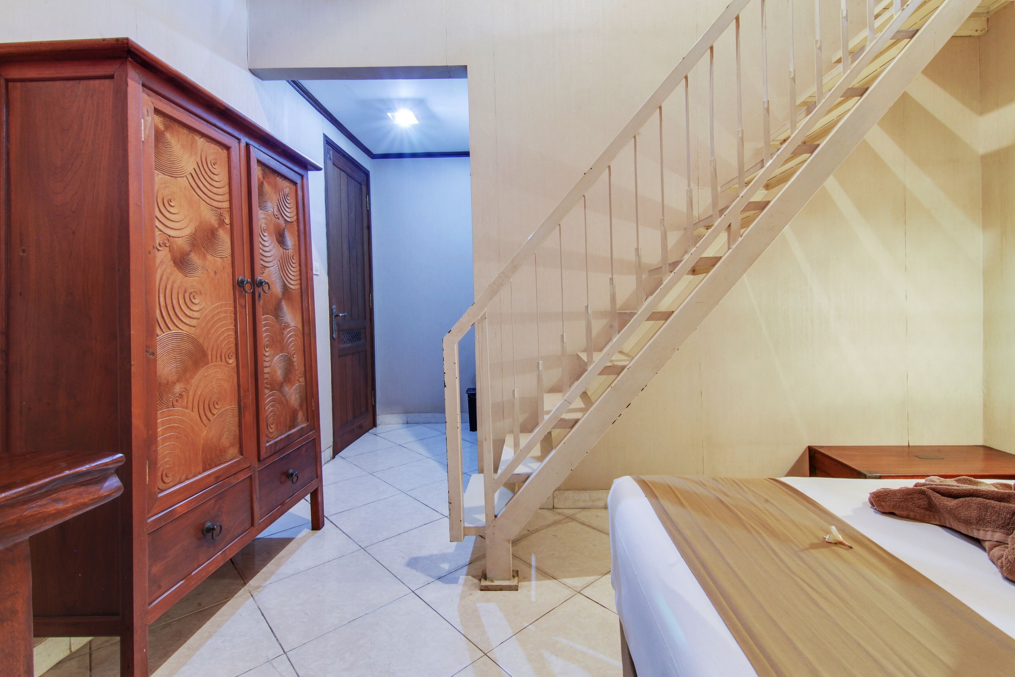A hotel room with a wooden wardrobe, a bed with a brown blanket, and a wooden staircase.