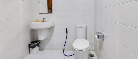 A small, clean bathroom with white tiles, a sink, a toilet, and a trash bin.