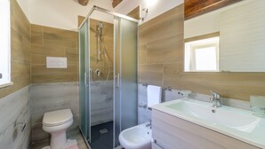 A modern bathroom with a glass-enclosed shower, a toilet, a bidet, and a sink with a mirror above. - Villa Ariana - Standard Room (Gatto Corvino)