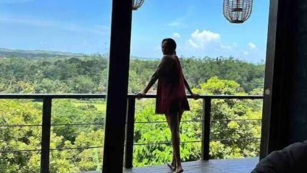 A person standing on a balcony with a view of a forested landscape.