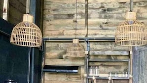 A rustic kitchen with wooden walls, a black countertop, and three wicker pendant lights.