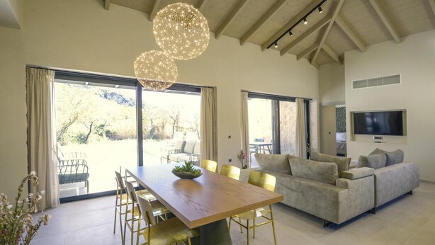 A spacious living area with a wooden dining table, a sofa, and a TV mounted on the wall. - Villa Selena in Ionian Islands (Kefalonia)