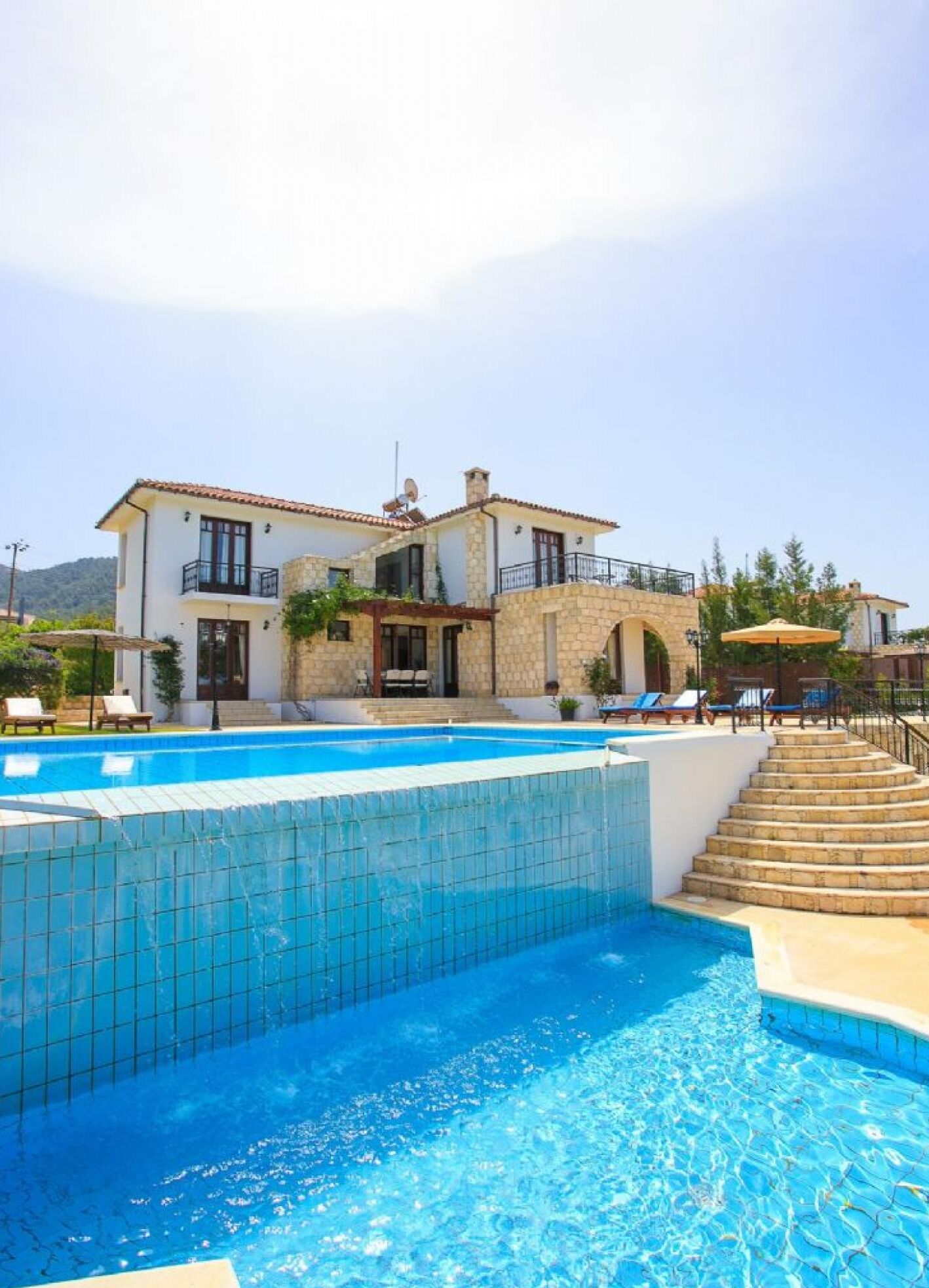 A two-story house with a swimming pool, stone exterior, and a balcony.