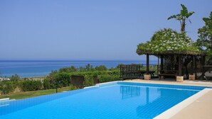 A rectangular swimming pool with clear blue tiles, surrounded by a wooden deck and a gazebo with a view of the sea. - Villa Ariadne in Argaka (Argaka)
