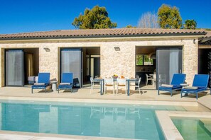 Relax by the pool surrounded by a Mediterranean-inspired building with large windows and sliding doors.