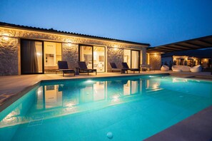 Relax by the rectangular pool surrounded by lounge chairs and a stone-clad building with large glass doors.