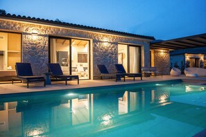 A swimming pool with lounge chairs and a stone building with large windows.