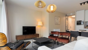 A modern living room with a flat-screen TV, sofa, chairs, and a dining area with a table and chairs. - Casselbergh Residences Sky Bridge (Ostend)