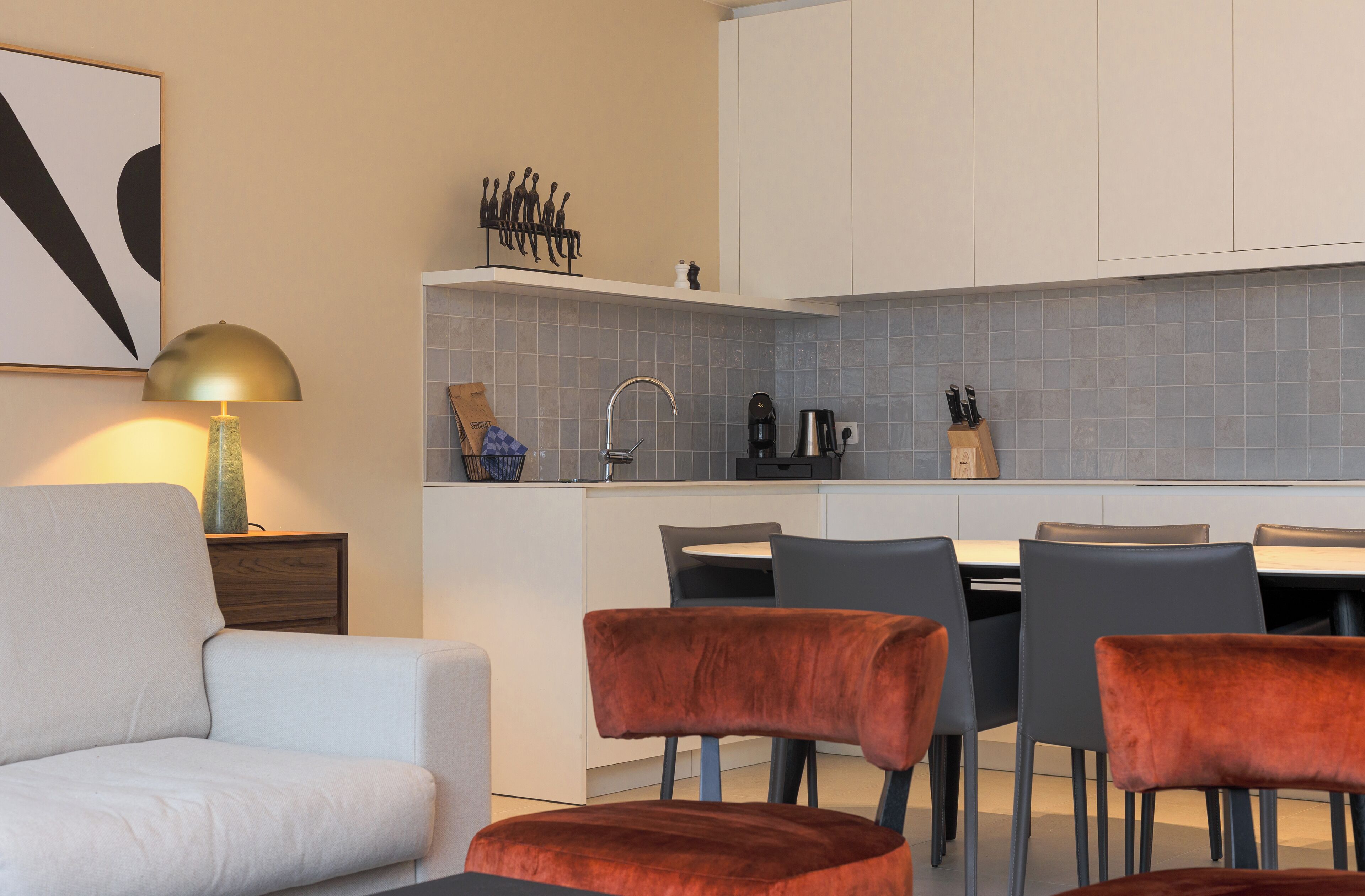 Een moderne keuken met witte kasten, een betegelde spatwand en een eethoek met grijze stoelen.