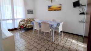 A dining area with a table and chairs, a painting on the wall, and a TV mounted on the wall. - Bright House With Garden Near to the Beach - Beahost (San Michele al Tagliamento)