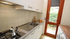 A kitchen with white cabinets, a stainless steel sink, a coffee maker, and a wooden door leading to a balcony. - Bright House With Garden Near to the Beach - Beahost (San Michele al Tagliamento)