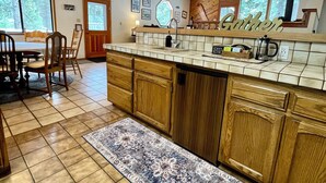 A spacious kitchen with wooden cabinets, a large island, and a view of the forest through the windows. - “Big Trees Retreat,” Boasts 5BR/2.5BA, Sleeps-16. 2-level living. Dog friendly! (Camp Connell)