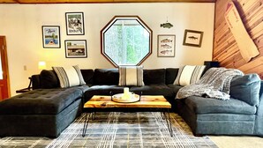 A cozy living room with a wooden ceiling, a large octagonal window, and a black and white patterned rug. - “Big Trees Retreat,” Boasts 5BR/2.5BA, Sleeps-16. 2-level living. Dog friendly! (Camp Connell)