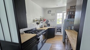 Eine moderne Küche mit schwarzen Schränken, einer Holz Arbeitsplatte und einer zentralen Kochinsel. Ein Herd, ein Backofen und eine Spüle sind vorhanden. Die Küche verfügt über eine geflieste Spritzschutzwand und ein Fenster, das für natürliches Licht sorgt.