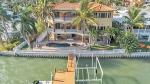 A multi-story house with a pool, surrounded by palm trees and a dock.